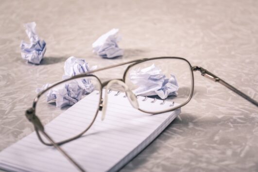Glasses sitting on a notepad with wads of crumpled up paper scattered as worker struggles with feeling off